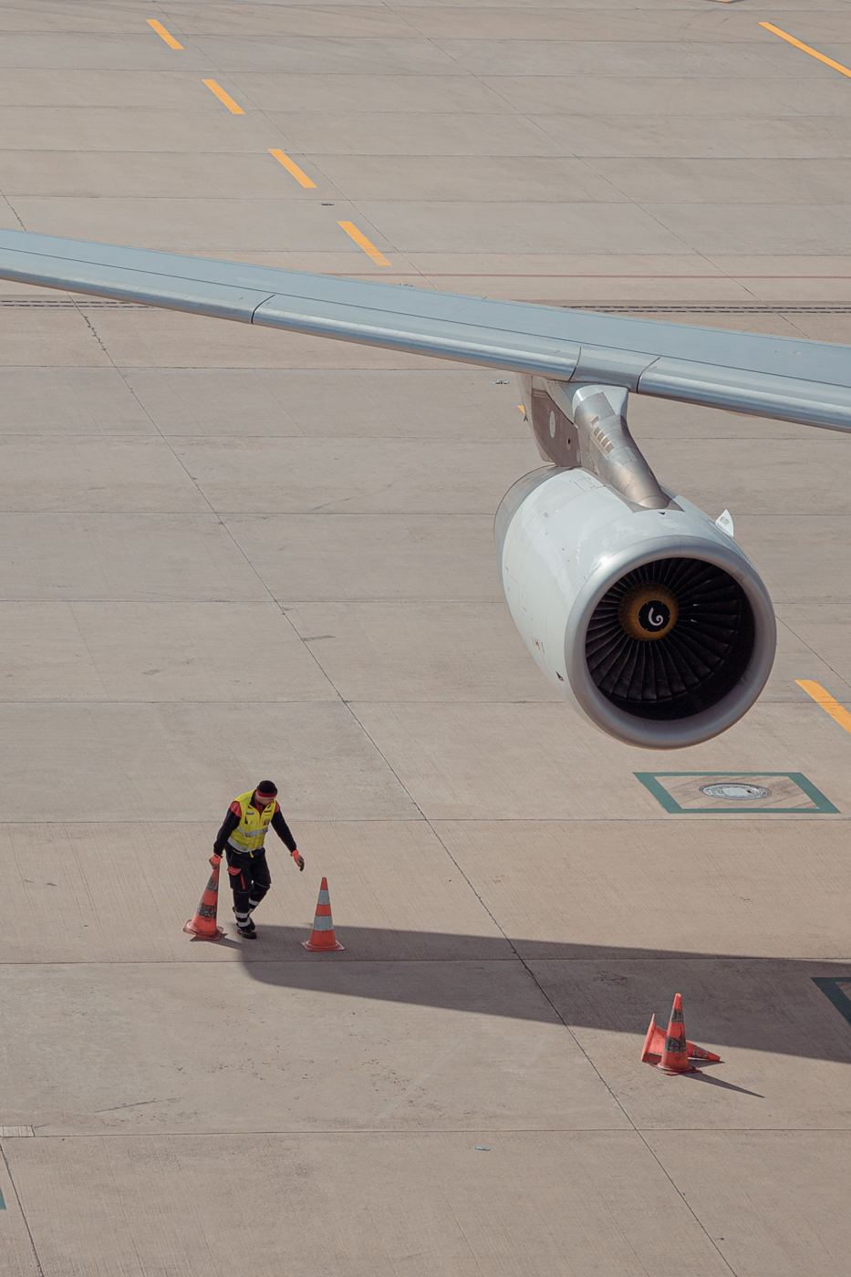 A ramp worker placing safety cones under an aircraft wing