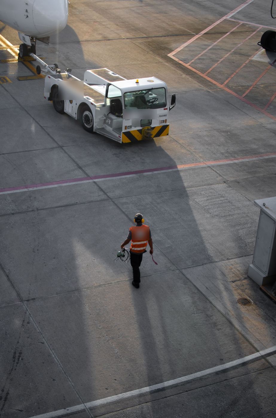 A ramp worker carrying a headset across the apron towards a pushback tug